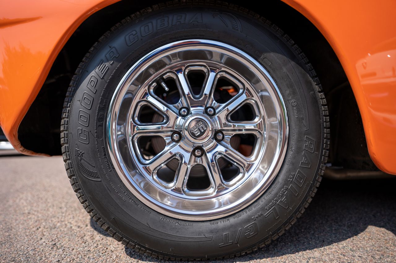 Close-up of a chrome wheel on a classic orange car, showcasing vintage style.